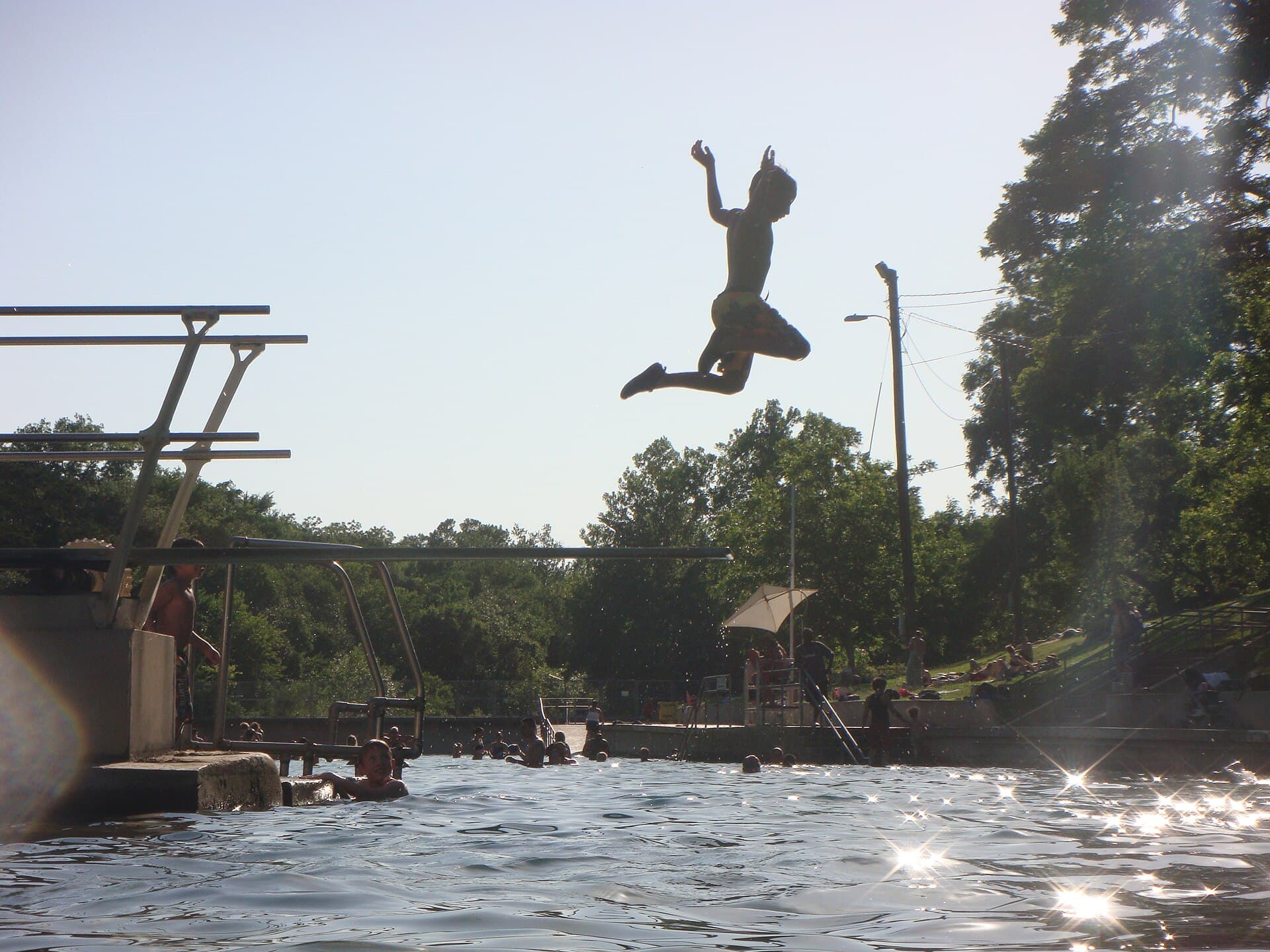 Swimmer mid-jump off the diving board at Barton Springs Pool in Austin on a summer afternoon