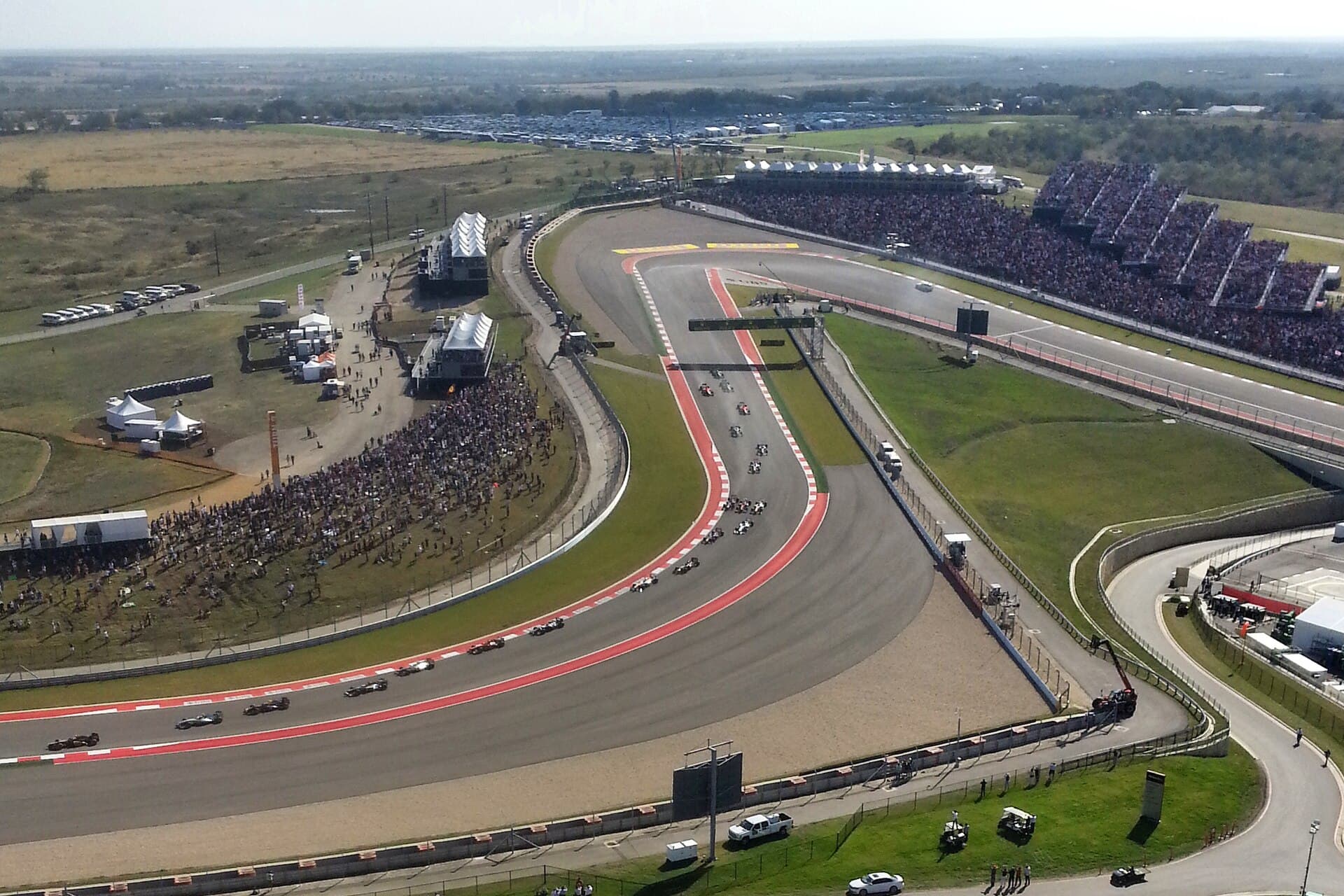 Aerial view of the US Grand Prix field streaming through COTA's esses, grandstands full and open ranchland beyond